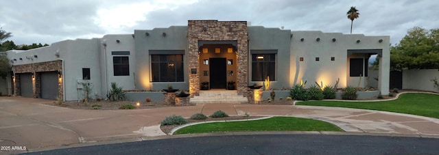 adobe home with stone siding, stucco siding, curved driveway, and a garage