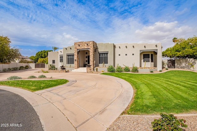 pueblo revival-style home with stone siding, stucco siding, a front yard, and fence