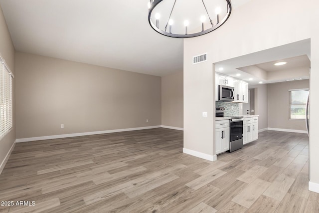 kitchen with decorative backsplash, white cabinets, light hardwood / wood-style flooring, and stainless steel appliances