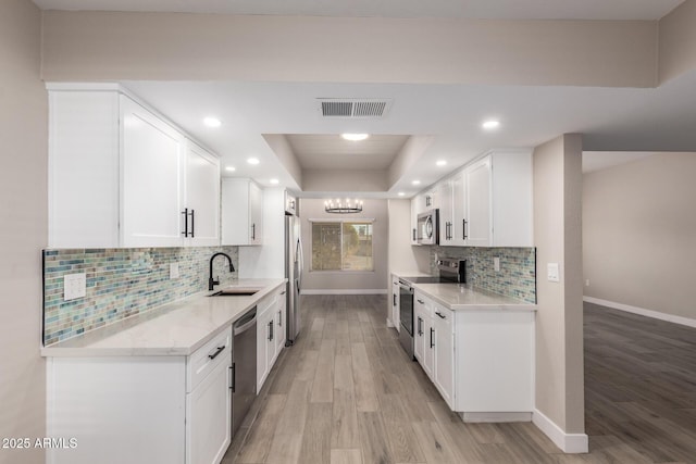 kitchen with white cabinetry, appliances with stainless steel finishes, a raised ceiling, light wood-type flooring, and sink