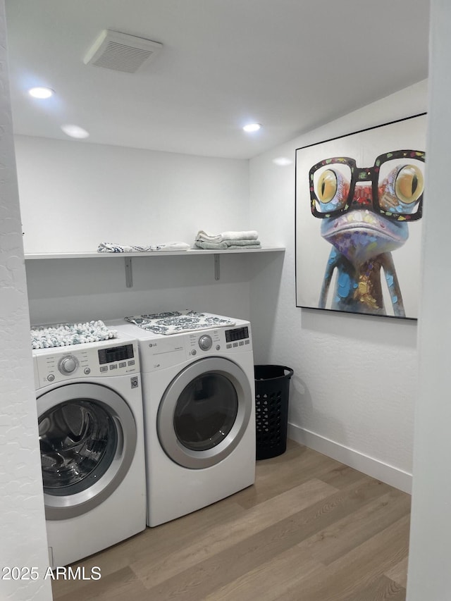 clothes washing area featuring washer and clothes dryer, wood finished floors, laundry area, visible vents, and baseboards