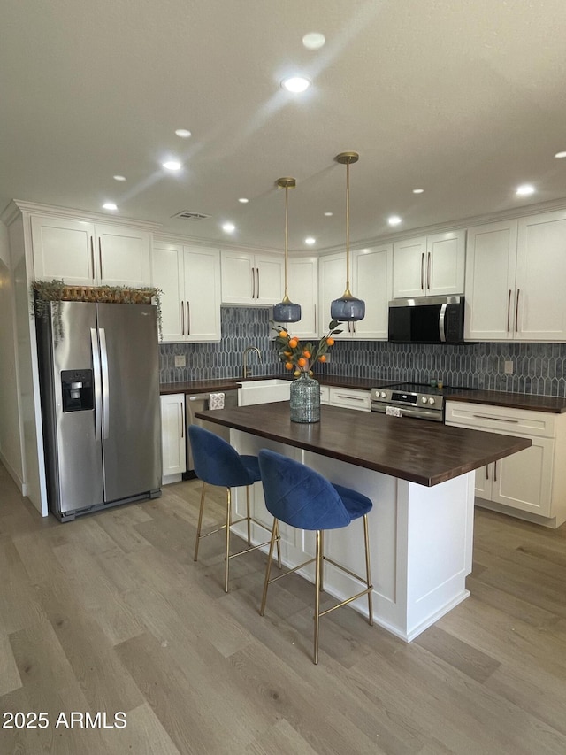 kitchen with light wood finished floors, wooden counters, white cabinetry, appliances with stainless steel finishes, and tasteful backsplash