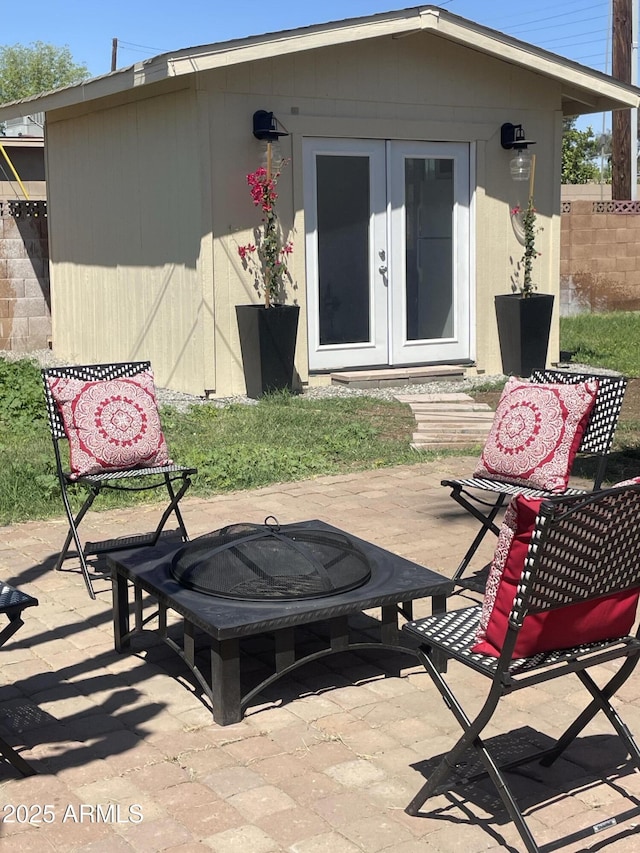 rear view of property with fence, a fire pit, french doors, a patio, and an outbuilding