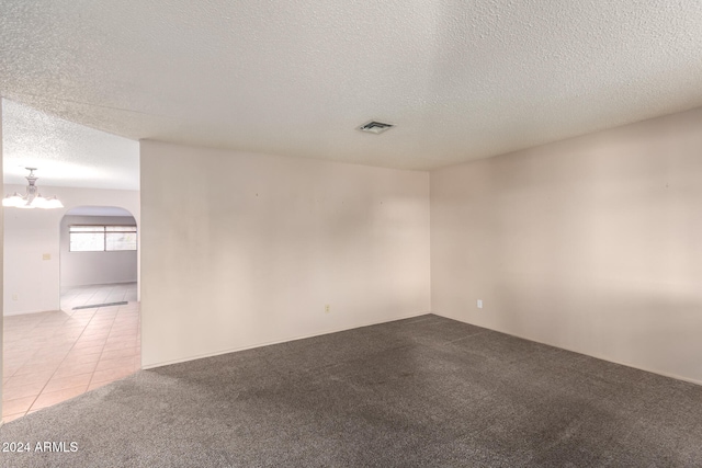 carpeted spare room featuring a textured ceiling and a chandelier