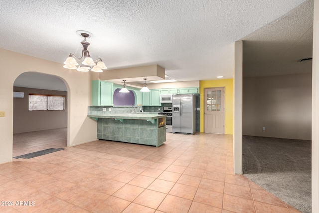 kitchen with decorative backsplash, kitchen peninsula, green cabinets, light tile patterned floors, and appliances with stainless steel finishes