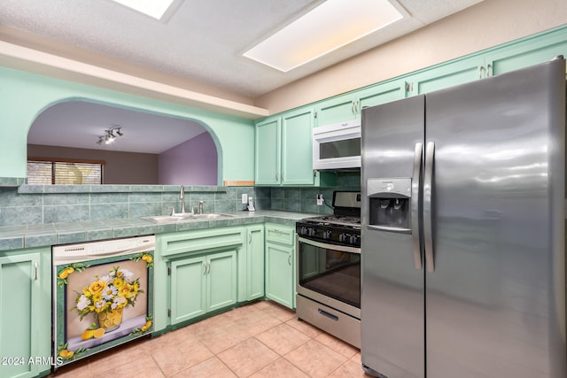 kitchen featuring tasteful backsplash, appliances with stainless steel finishes, sink, green cabinetry, and light tile patterned floors