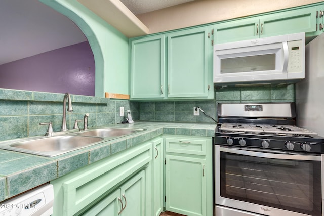 kitchen featuring sink, green cabinetry, backsplash, stainless steel range with gas stovetop, and dishwashing machine