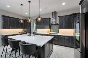 kitchen featuring recessed lighting, a kitchen island with sink, a kitchen breakfast bar, wall chimney exhaust hood, and light countertops