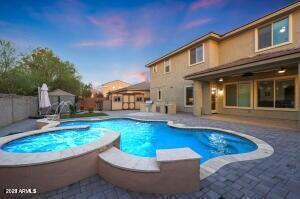 pool at dusk featuring a patio, a fenced backyard, and a pool with connected hot tub