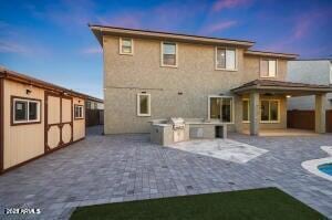 back of property at dusk with fence, an outdoor pool, exterior kitchen, and a patio