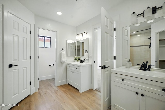full bathroom featuring two vanities, a sink, tiled shower, baseboards, and wood finished floors