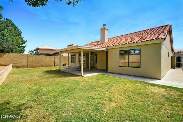 back of house with a tile roof, a chimney, a lawn, fence, and a patio