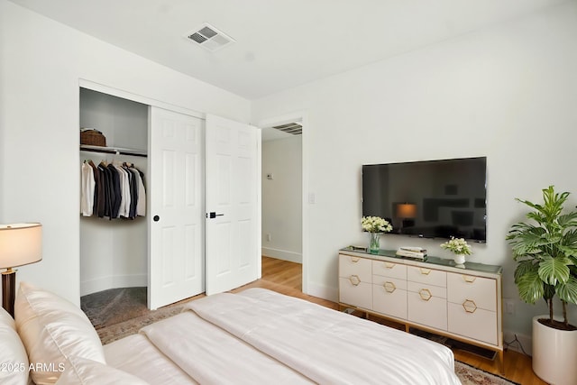 bedroom featuring baseboards, wood finished floors, visible vents, and a closet