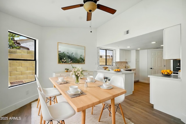 dining space featuring light wood-style flooring, baseboards, visible vents, lofted ceiling, and ceiling fan