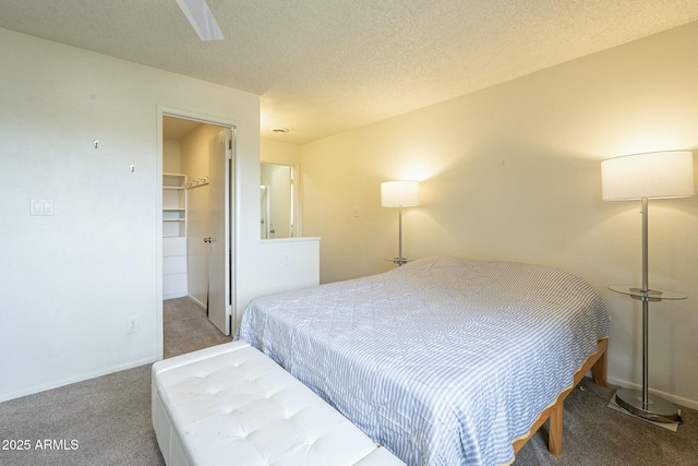 carpeted bedroom with a textured ceiling, a closet, a walk in closet, and baseboards