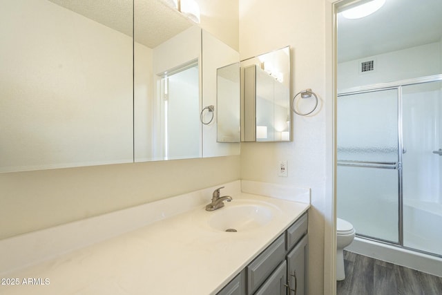 bathroom featuring a stall shower, visible vents, toilet, wood finished floors, and vanity