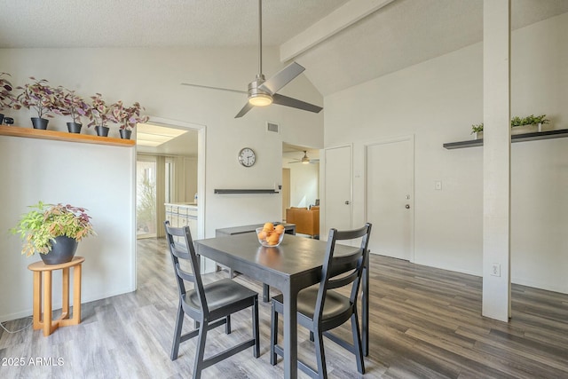 dining area with visible vents, wood finished floors, a textured ceiling, high vaulted ceiling, and beam ceiling