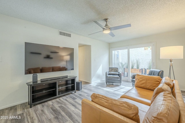 living area featuring a textured ceiling, wood finished floors, visible vents, and baseboards