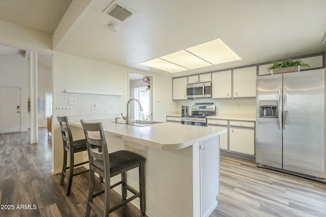 kitchen with stainless steel appliances, a sink, visible vents, light wood-style floors, and light countertops