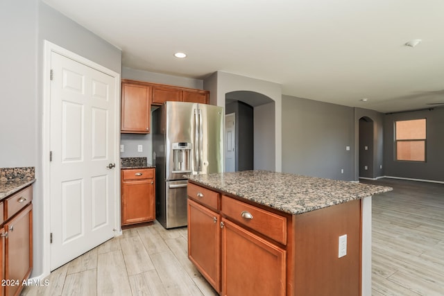 kitchen featuring light wood-type flooring, stainless steel fridge with ice dispenser, a center island, and dark stone countertops