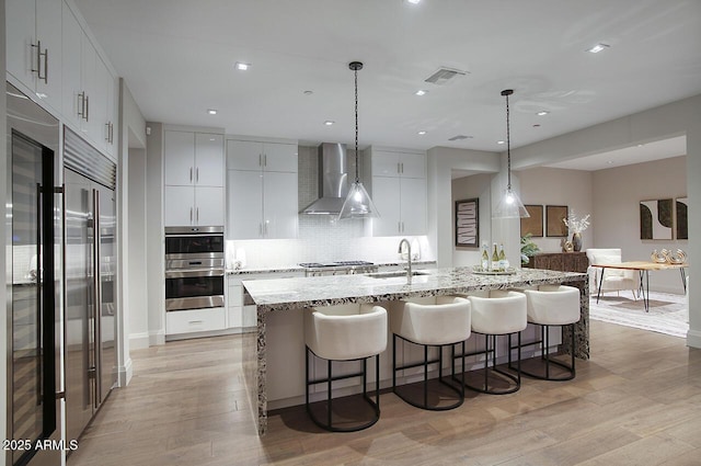 kitchen with light wood-style flooring, stainless steel appliances, a sink, visible vents, and wall chimney range hood