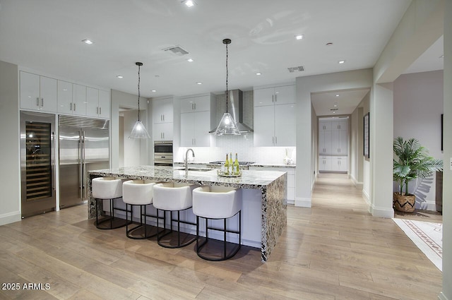 kitchen featuring visible vents, light wood-style floors, appliances with stainless steel finishes, wall chimney range hood, and a sink