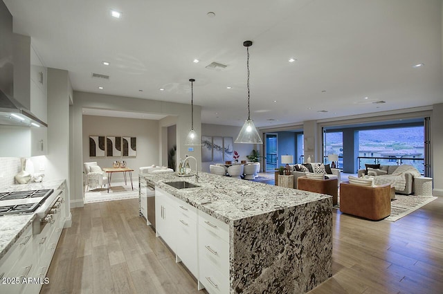 kitchen with visible vents, light wood-style flooring, stainless steel appliances, wall chimney range hood, and a sink