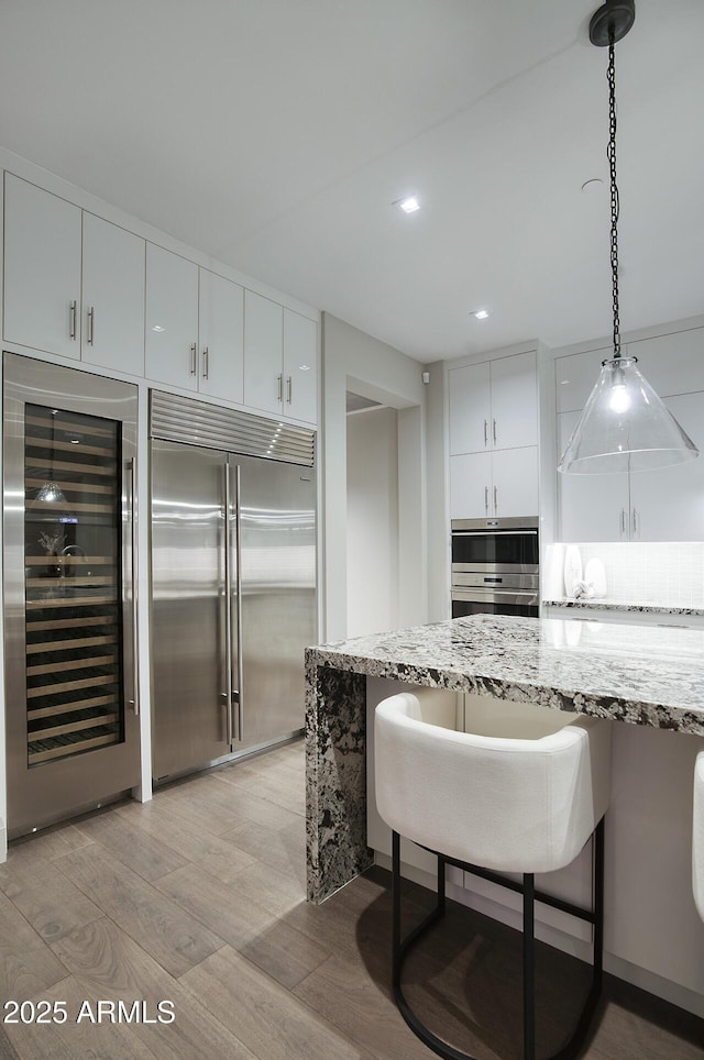 kitchen with wine cooler, light stone counters, a kitchen breakfast bar, built in refrigerator, and pendant lighting