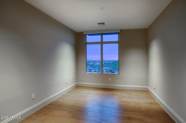 spare room with light wood finished floors, visible vents, and baseboards