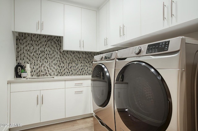 laundry room featuring a sink, light wood finished floors, washer and clothes dryer, and cabinet space