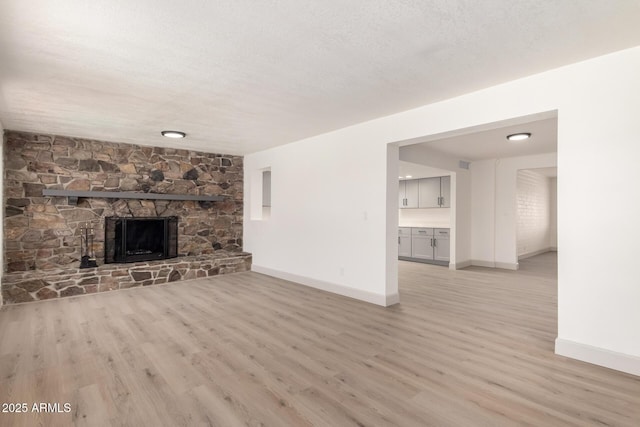 unfurnished living room featuring light wood-type flooring, a stone fireplace, and a textured ceiling