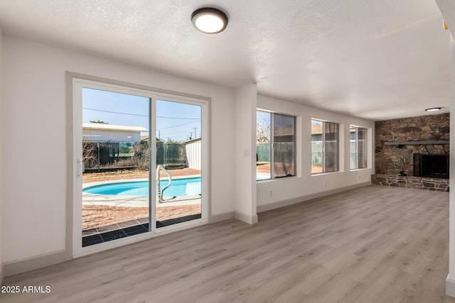 unfurnished living room with a textured ceiling, light hardwood / wood-style floors, and a stone fireplace