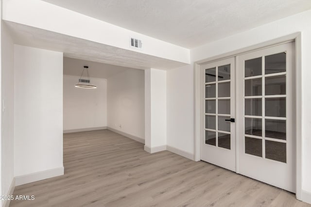 unfurnished room with a textured ceiling, light hardwood / wood-style floors, and french doors