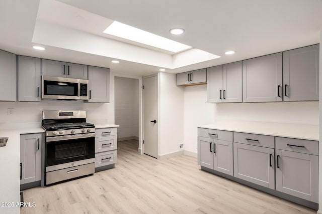 kitchen featuring light wood-type flooring, stainless steel appliances, gray cabinetry, and a raised ceiling