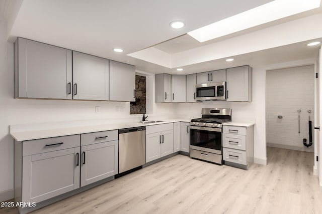 kitchen with a skylight, light hardwood / wood-style floors, gray cabinets, stainless steel appliances, and sink