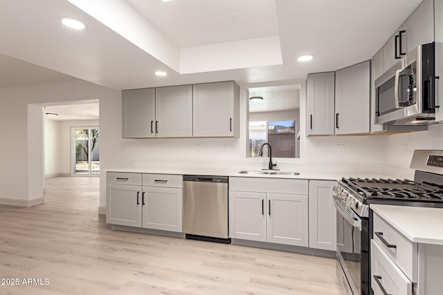 kitchen featuring gray cabinets, stainless steel appliances, a tray ceiling, light hardwood / wood-style flooring, and sink