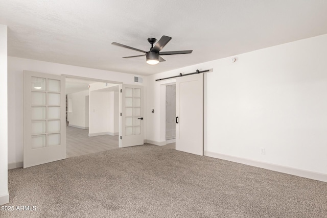 spare room featuring ceiling fan, a barn door, french doors, and light colored carpet