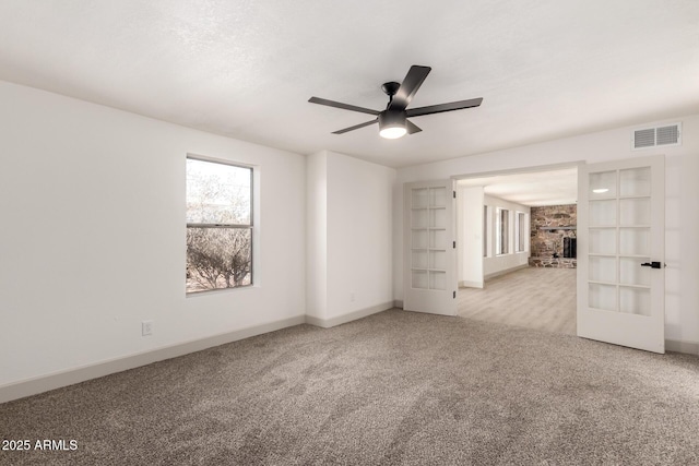 carpeted spare room featuring ceiling fan, a stone fireplace, and french doors