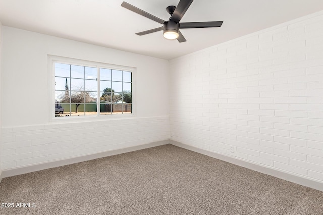 spare room featuring ceiling fan, carpet, and brick wall