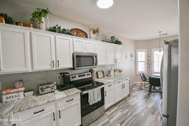 kitchen featuring pendant lighting, stainless steel appliances, tasteful backsplash, light stone countertops, and white cabinets