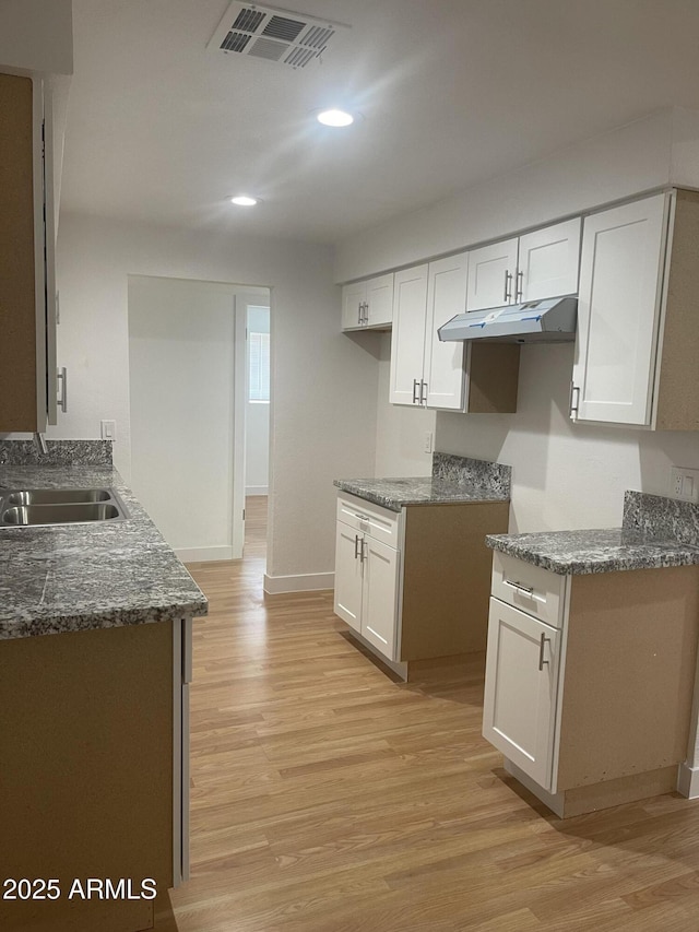 kitchen featuring white cabinets, light wood-type flooring, dark stone countertops, and sink