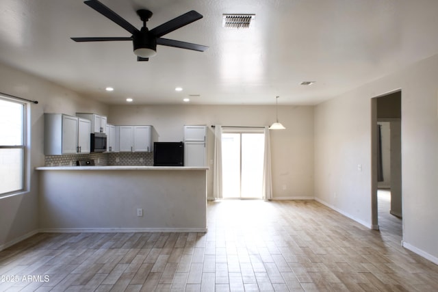 kitchen featuring stainless steel microwave, hanging light fixtures, light countertops, fridge, and white cabinetry