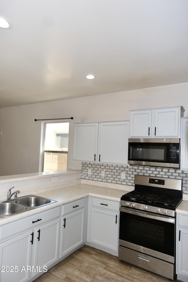 kitchen featuring stainless steel appliances, light countertops, a sink, and white cabinetry