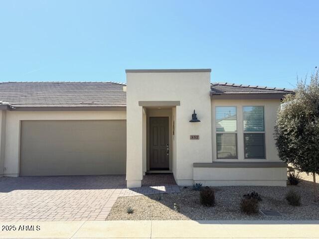 view of front of home with decorative driveway, an attached garage, and stucco siding