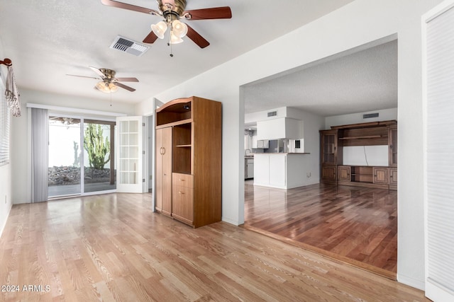 unfurnished living room featuring ceiling fan, light hardwood / wood-style floors, and a textured ceiling