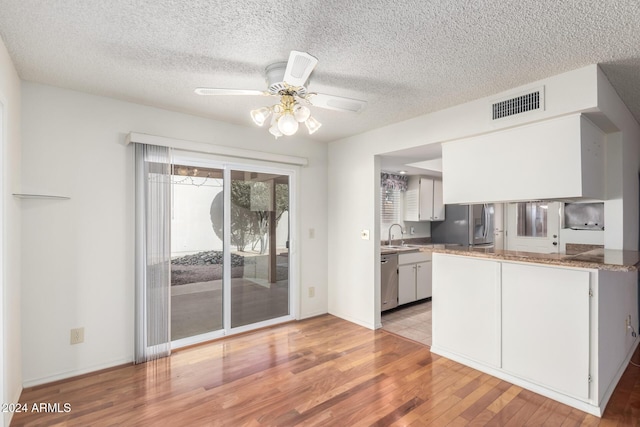 kitchen with light hardwood / wood-style flooring, white cabinets, a textured ceiling, and appliances with stainless steel finishes