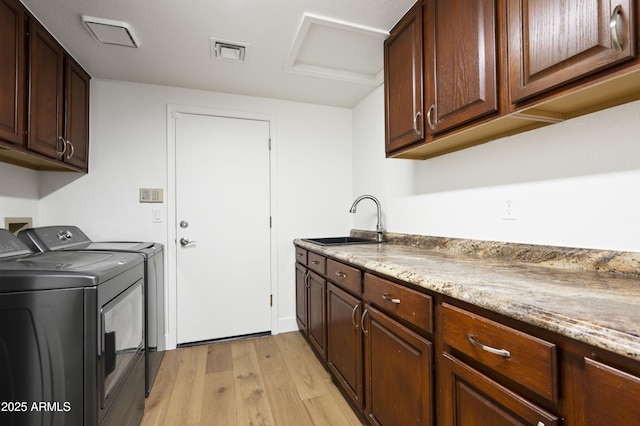 washroom with visible vents, washing machine and clothes dryer, cabinet space, a sink, and light wood-style floors