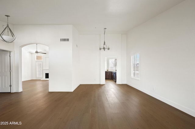 unfurnished dining area featuring visible vents, baseboards, arched walkways, a high ceiling, and dark wood-style floors