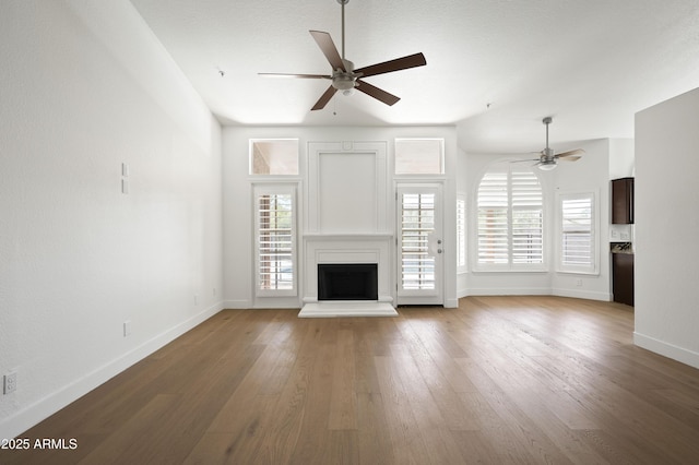 unfurnished living room featuring baseboards, a fireplace with raised hearth, ceiling fan, and hardwood / wood-style flooring