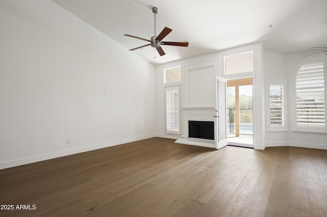 unfurnished living room with a fireplace with raised hearth, wood finished floors, baseboards, and ceiling fan